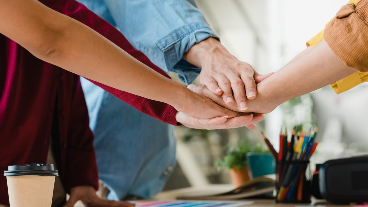 Asian businessmen and businesswomen meeting brainstorming putting hands up for new startup and giving strength motivation working together in modern creative office. Coworker teamwork concept.